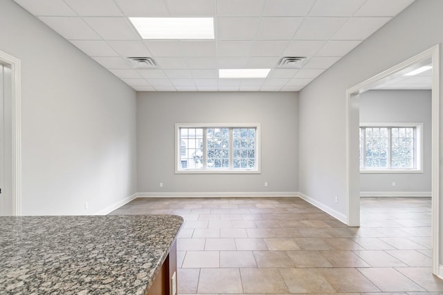 empty room featuring a paneled ceiling, a wealth of natural light, and light tile patterned flooring