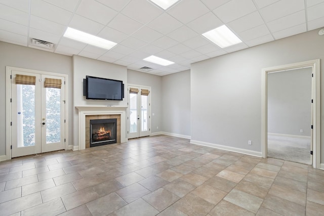 unfurnished living room featuring a tile fireplace, french doors, and a drop ceiling