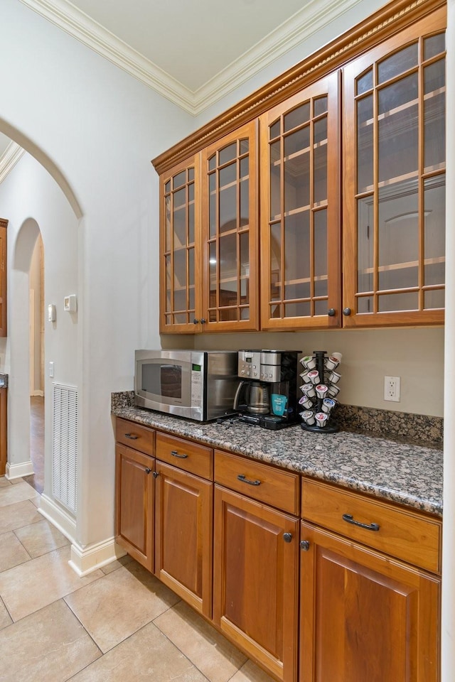 bar featuring dark stone countertops, light tile patterned flooring, and ornamental molding