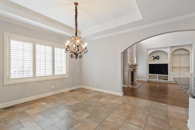 empty room featuring a notable chandelier, built in features, crown molding, and a tray ceiling