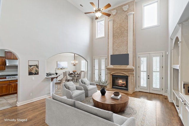 living room with ceiling fan with notable chandelier, a high ceiling, light wood-type flooring, and plenty of natural light