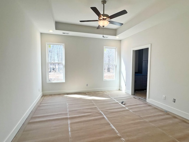 empty room with ceiling fan, visible vents, baseboards, and a raised ceiling