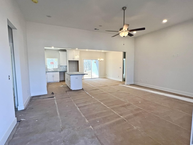 unfurnished living room featuring a towering ceiling, recessed lighting, baseboards, and ceiling fan with notable chandelier