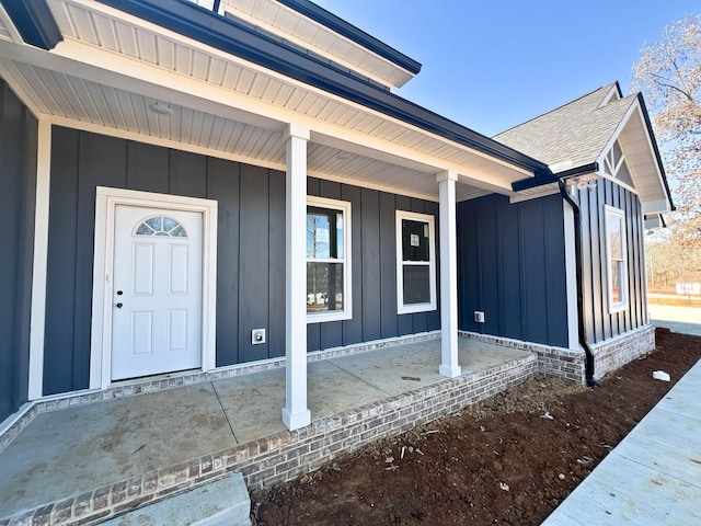 doorway to property with board and batten siding, a porch, and a shingled roof