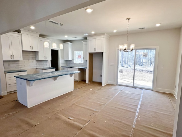 kitchen featuring visible vents, dark countertops, a center island, hanging light fixtures, and white cabinetry