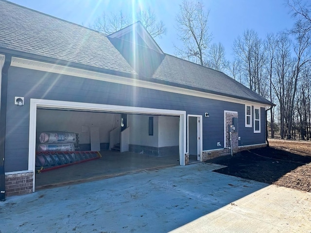 back of house featuring driveway, stone siding, a shingled roof, and a garage