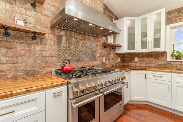 kitchen featuring wall chimney range hood, dark hardwood / wood-style flooring, butcher block countertops, backsplash, and double oven range