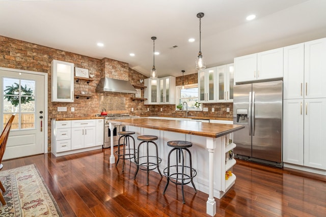 kitchen with butcher block counters, a center island, stainless steel appliances, wall chimney range hood, and white cabinets