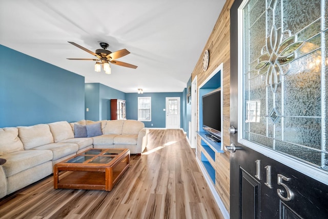 living room featuring wood-type flooring, ceiling fan, and wooden walls