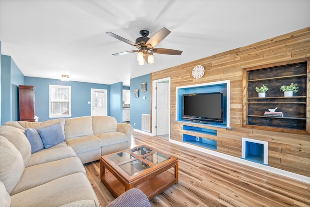 living room featuring hardwood / wood-style flooring, ceiling fan, and wood walls