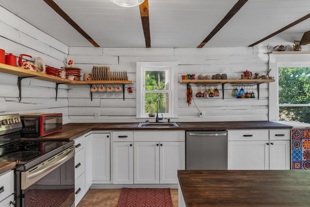 kitchen featuring stainless steel appliances, white cabinetry, wooden walls, and sink