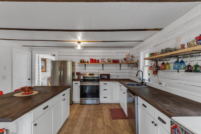 kitchen with sink, wood counters, appliances with stainless steel finishes, white cabinets, and light wood-type flooring