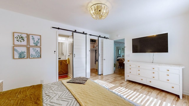 bedroom with a barn door, light hardwood / wood-style floors, ensuite bath, and a closet