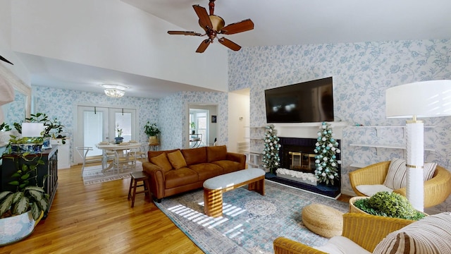 living room featuring french doors, ceiling fan, high vaulted ceiling, a fireplace, and light hardwood / wood-style floors