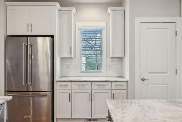 kitchen featuring white cabinetry, high quality fridge, backsplash, and light stone countertops