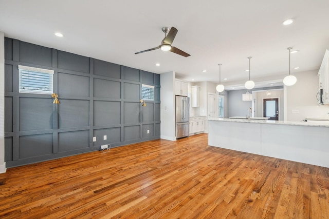 kitchen featuring stainless steel refrigerator, white cabinetry, light hardwood / wood-style flooring, and decorative light fixtures