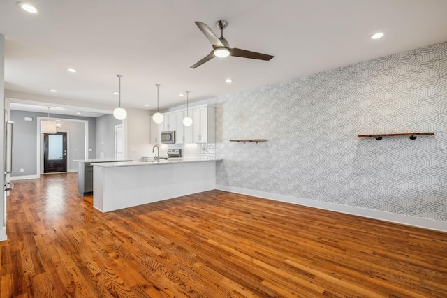 kitchen with decorative light fixtures, light countertops, stainless steel microwave, a peninsula, and wallpapered walls