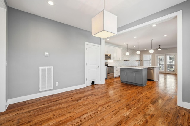 kitchen with decorative light fixtures, stainless steel appliances, light countertops, visible vents, and a kitchen island