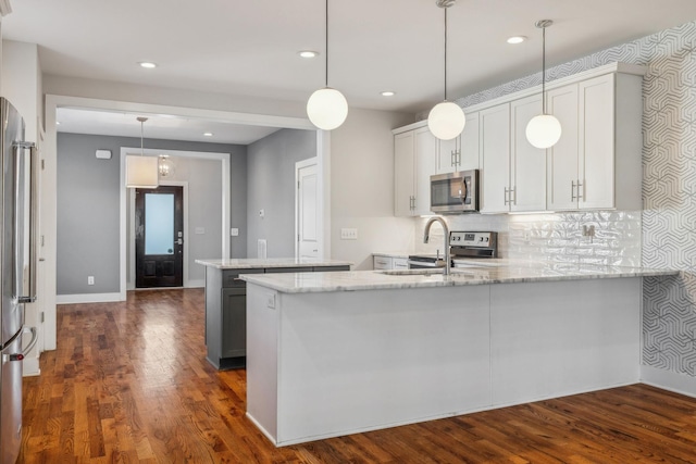 kitchen with kitchen peninsula, appliances with stainless steel finishes, decorative light fixtures, dark hardwood / wood-style floors, and white cabinetry