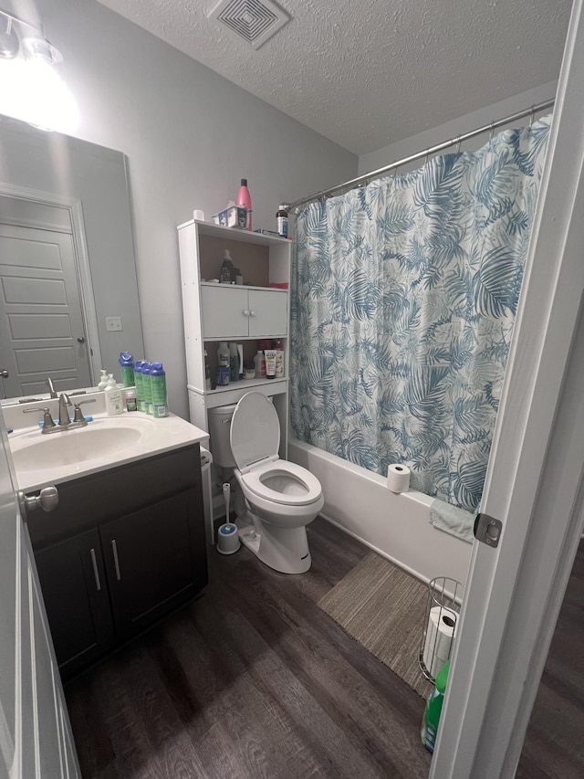 full bathroom with hardwood / wood-style floors, vanity, toilet, shower / bath combo with shower curtain, and a textured ceiling