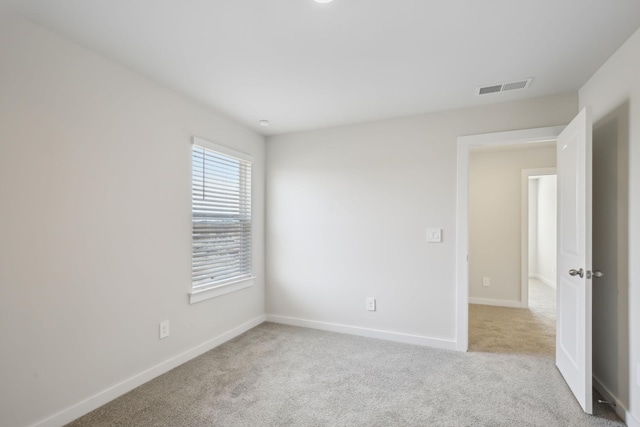 spare room featuring light carpet, visible vents, and baseboards