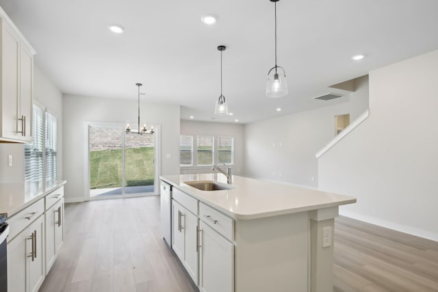 kitchen with light countertops, a sink, a kitchen island with sink, and pendant lighting