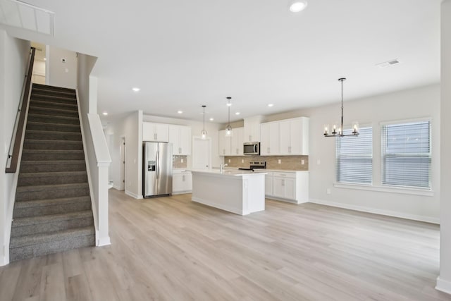 kitchen with hanging light fixtures, a kitchen island with sink, stainless steel appliances, light countertops, and white cabinetry