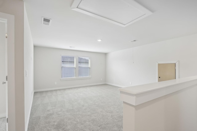 empty room with attic access, visible vents, baseboards, and light colored carpet