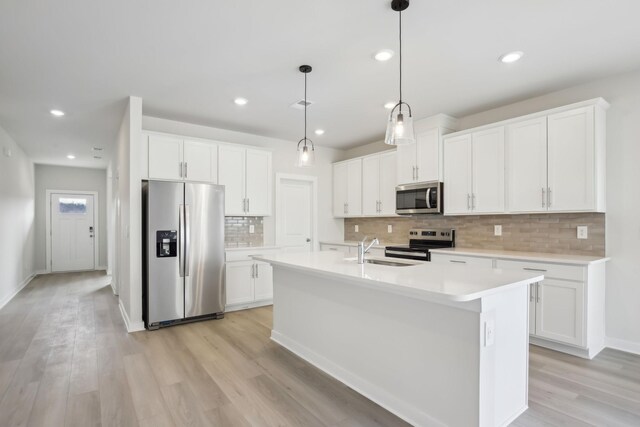 kitchen featuring decorative light fixtures, stainless steel appliances, light countertops, a kitchen island with sink, and white cabinets