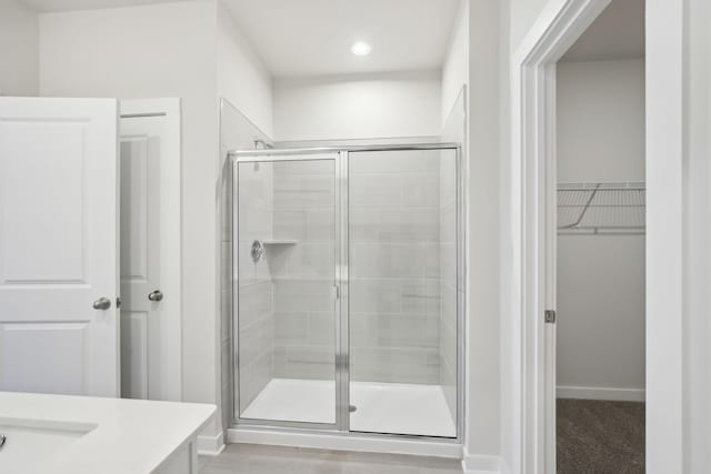 bathroom with a stall shower, a walk in closet, vanity, and baseboards