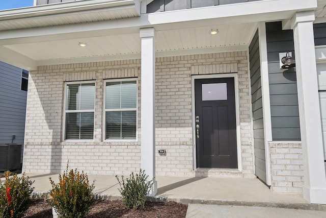 property entrance featuring central AC unit, a porch, and brick siding