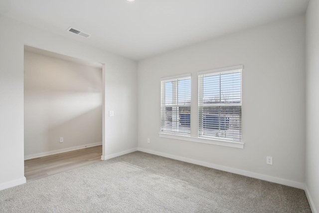 empty room with baseboards, visible vents, and light colored carpet