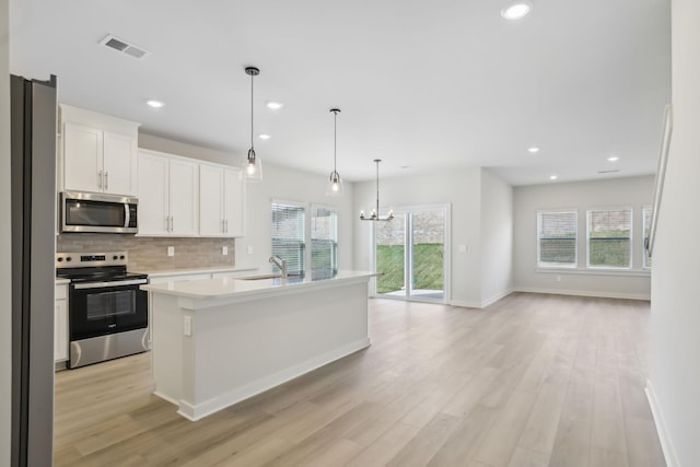 kitchen featuring a kitchen island with sink, stainless steel appliances, white cabinetry, light countertops, and decorative light fixtures