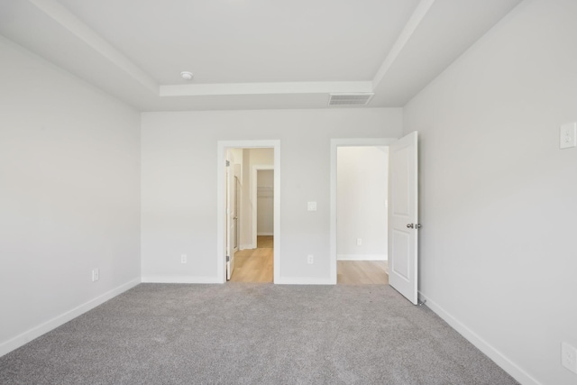 unfurnished bedroom with a raised ceiling, light carpet, visible vents, and baseboards