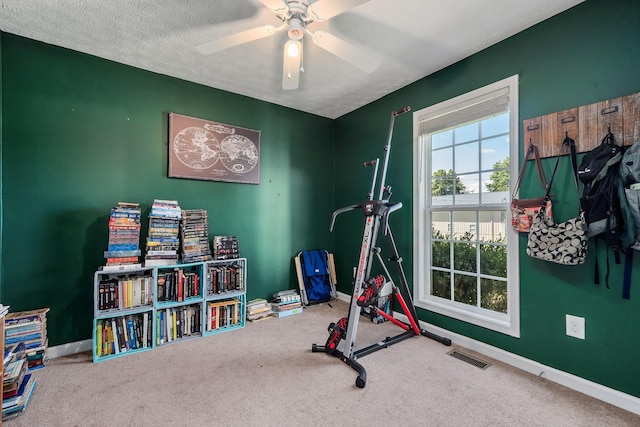 exercise area featuring ceiling fan, carpet, and a textured ceiling