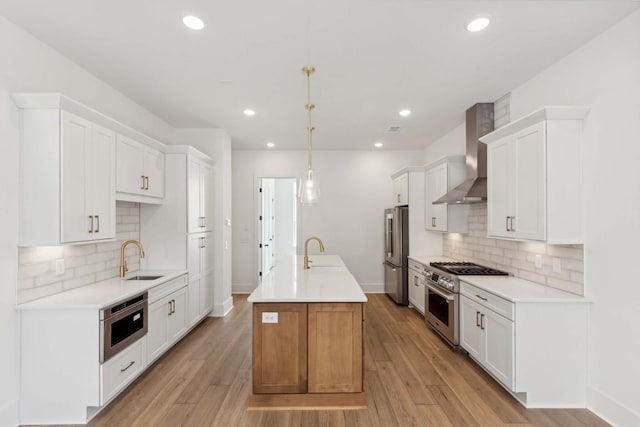 kitchen with appliances with stainless steel finishes, wall chimney exhaust hood, pendant lighting, light hardwood / wood-style flooring, and white cabinets