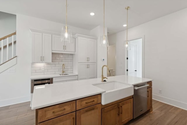 kitchen with light wood-type flooring, sink, a center island with sink, dishwasher, and white cabinetry