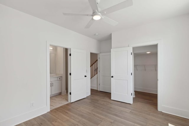 unfurnished bedroom featuring ceiling fan, a spacious closet, light hardwood / wood-style flooring, ensuite bathroom, and a closet