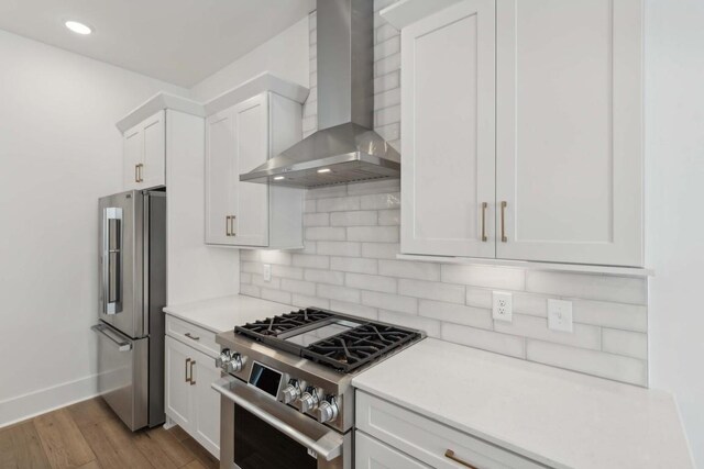 kitchen with white cabinets, wall chimney range hood, tasteful backsplash, premium appliances, and light hardwood / wood-style floors