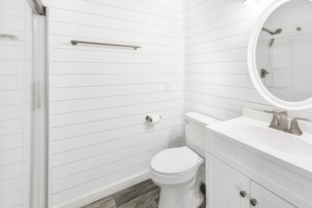 bathroom with walk in shower, toilet, wooden walls, vanity, and hardwood / wood-style flooring