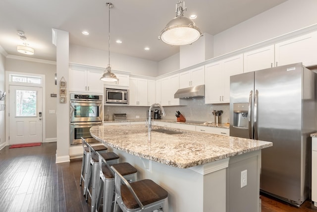 kitchen featuring white cabinetry, sink, stainless steel appliances, decorative light fixtures, and a center island with sink