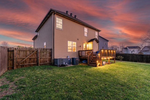 back house at dusk with a yard, central AC, and a deck