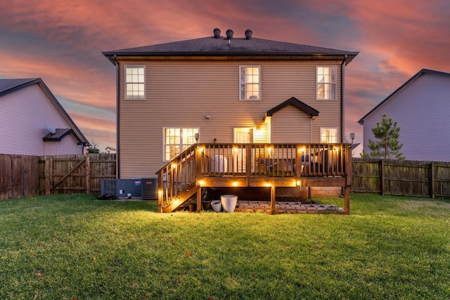 back house at dusk with central AC unit, a lawn, and a wooden deck