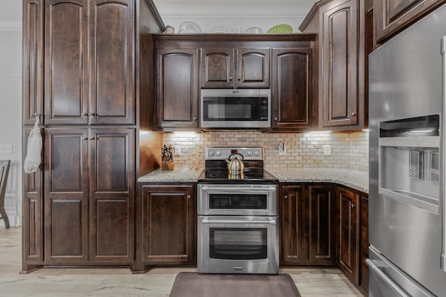 kitchen featuring light stone countertops, stainless steel appliances, decorative backsplash, dark brown cabinets, and ornamental molding