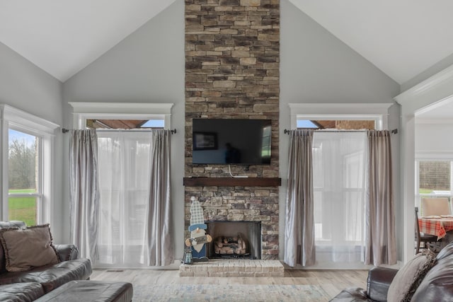 living room with a stone fireplace, high vaulted ceiling, and light hardwood / wood-style flooring