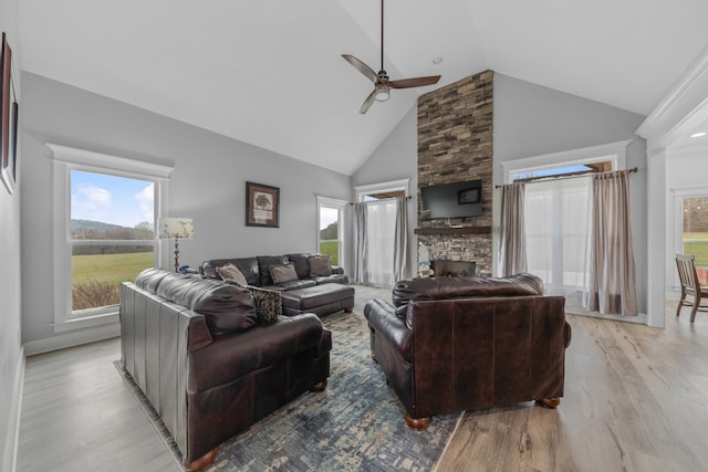 living room with plenty of natural light, a stone fireplace, light wood-type flooring, and high vaulted ceiling