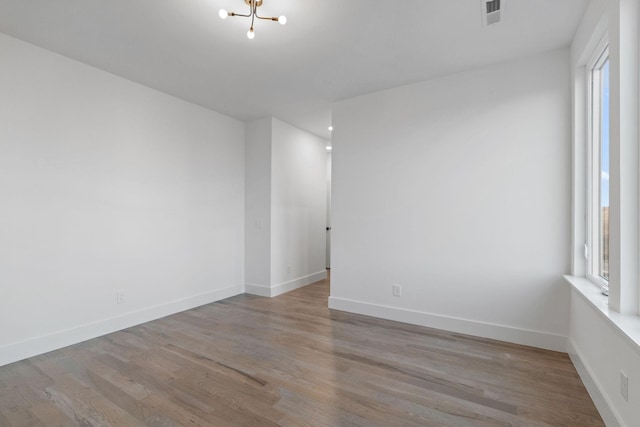 spare room with an inviting chandelier and light hardwood / wood-style floors