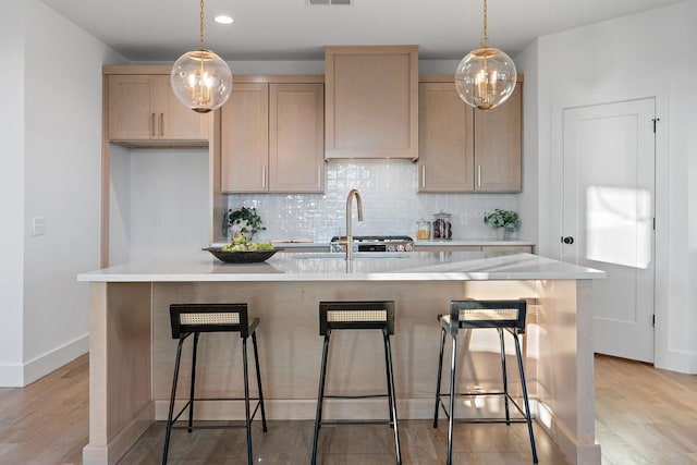 kitchen with hanging light fixtures, an island with sink, light brown cabinetry, decorative backsplash, and sink