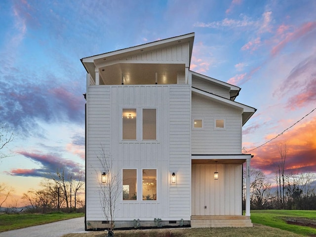 back house at dusk featuring a lawn and a balcony