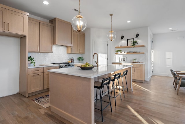 kitchen featuring a kitchen island with sink, hardwood / wood-style flooring, wall chimney exhaust hood, light brown cabinets, and tasteful backsplash